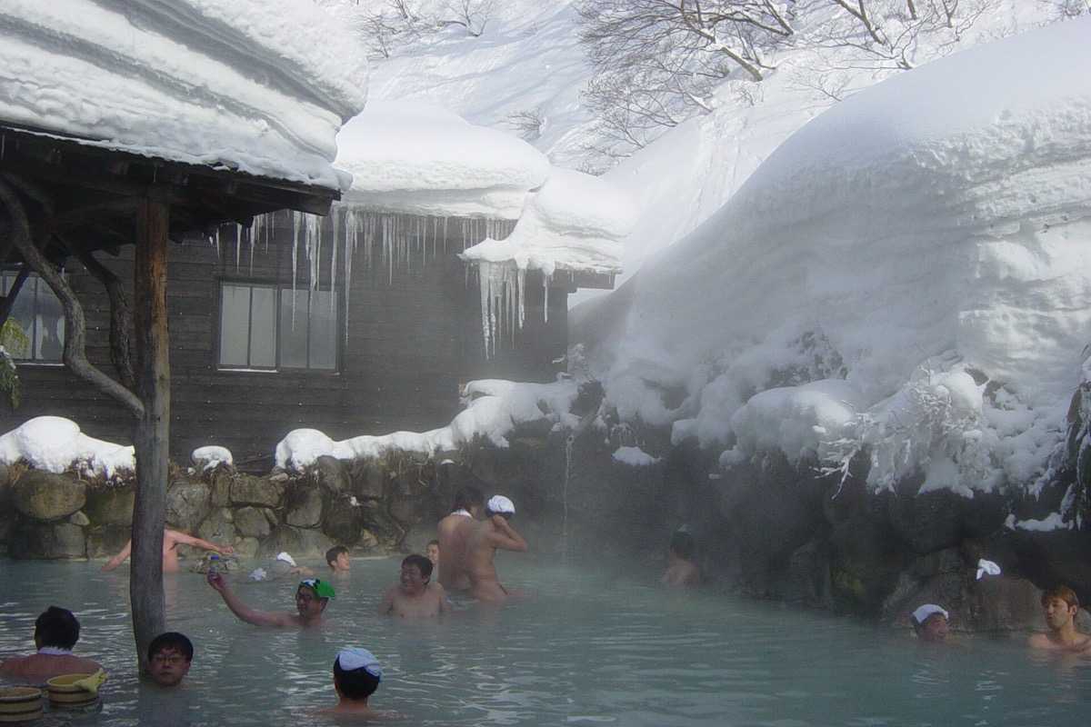 A steaming outdoor onsen bath surrounded by snow in winter